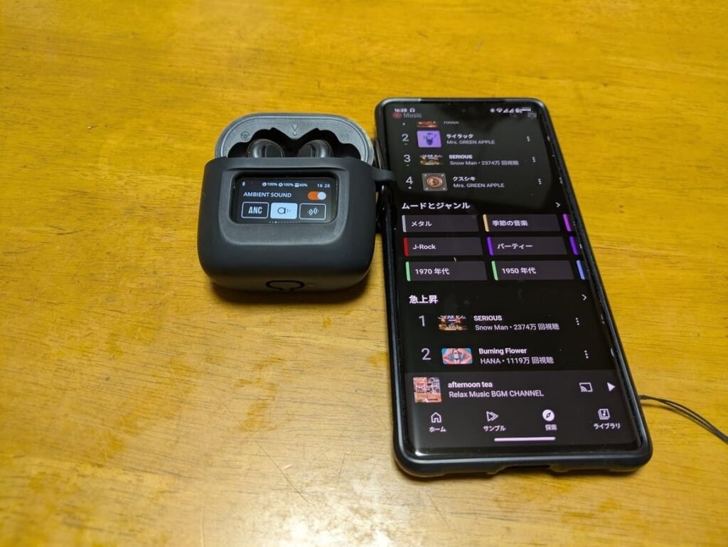 JBL TOUR PRO 2とスマホがテーブルに並べられている画像。JBL TOUR PRO 2を接続しスマホで音楽を聴くイメージ画像。