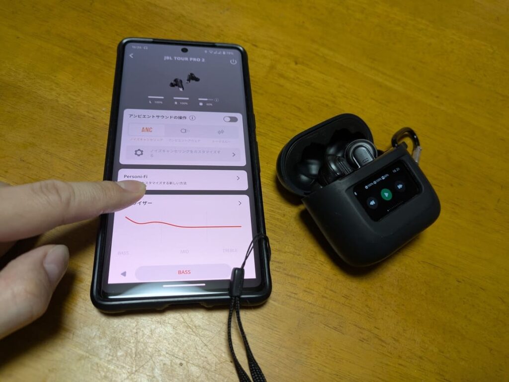 JBL TOUR PRO 2とスマホの画像。タッチディスプレイではなくスマホの画面を操作しているイメージ画像。