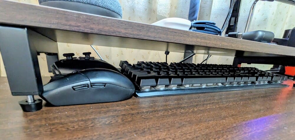 デスクシェルフの下にキーボードとマウスとゲーム用コントローラーが収納されている画像